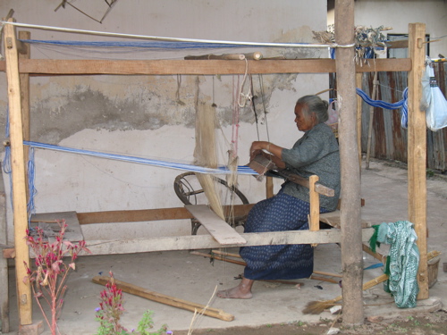 old woman weaving outside her house